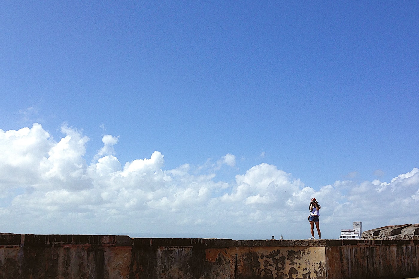 A figure photographing from a fort wall under a wide cloudy sky